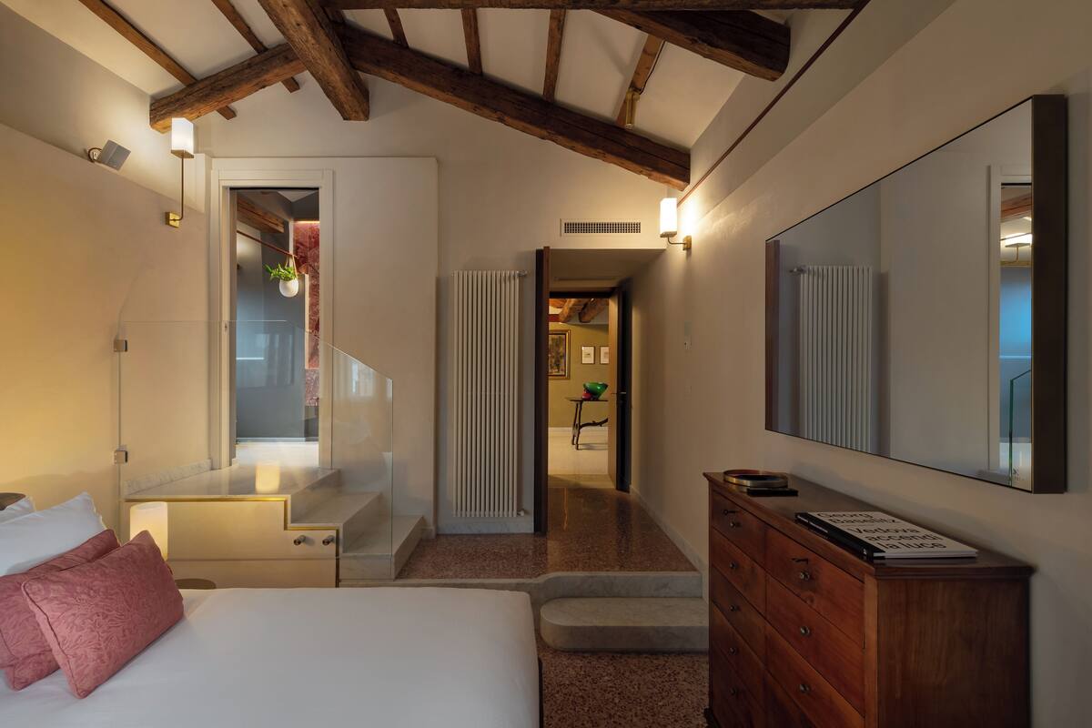 Ein Hotelzimmer mit Bett, Schminktisch, Spiegel und Blick auf einen Flur zum Badezimmer.