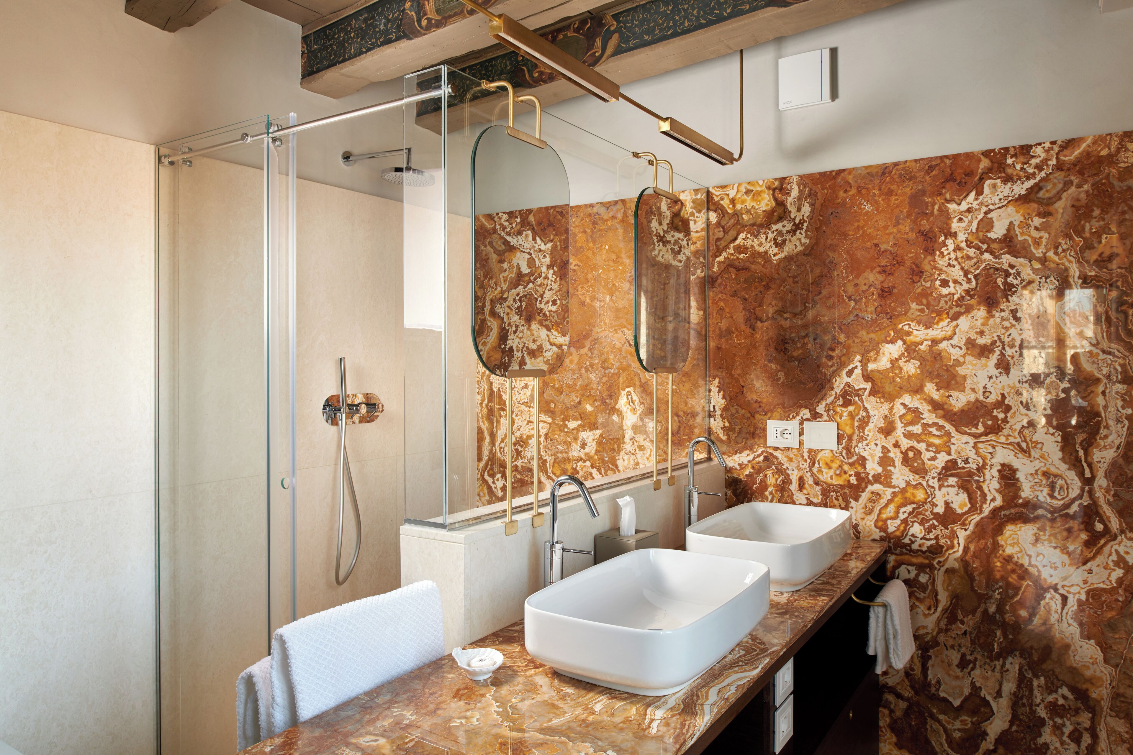 A modern bathroom with a glass-enclosed shower, two sinks, and a marble backsplash.