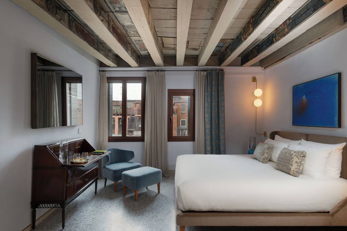 Ein Hotelzimmer mit Bett, Schreibtisch, zwei Stühlen, einem Schminktisch und einem großen Fenster mit Vorhängen.