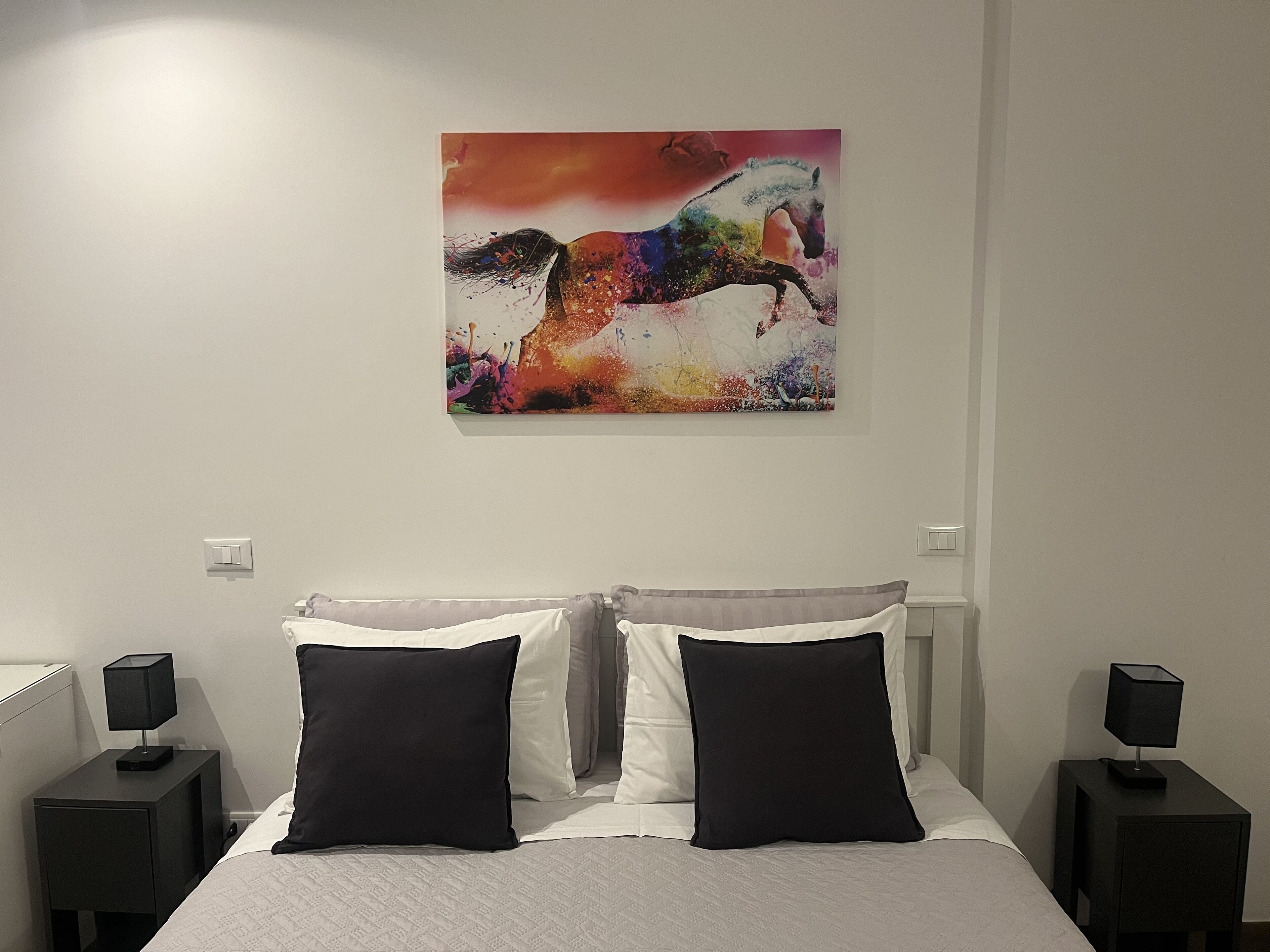 A modern bedroom with a bed, two nightstands, and a colorful abstract painting on the wall.