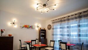 A dining area with a wooden table, chairs, a clock, a bookshelf, and a ceiling light fixture. - Anastasio Vatican Rooms (Rome)