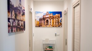 A narrow hallway with a white wall, a ceiling light, and a bookshelf with books. - Anastasio Vatican Rooms (Rome)