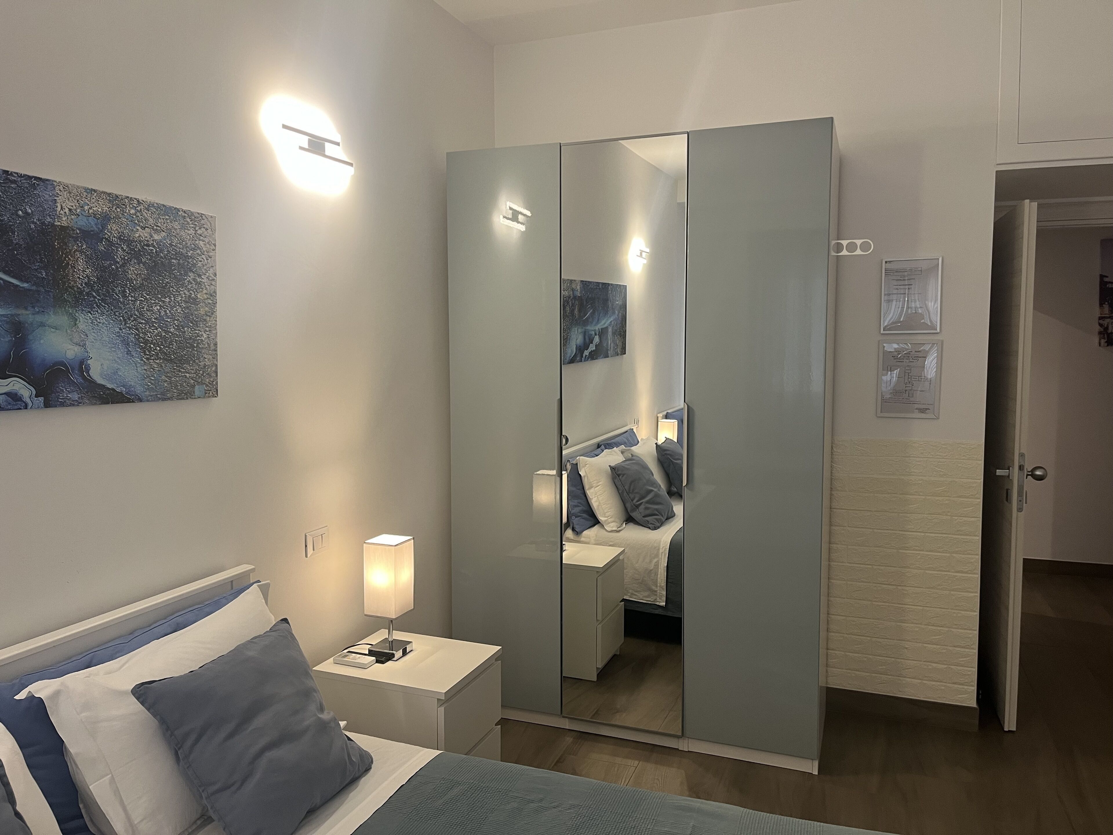 A bedroom with a bed, bedside table, lamp, and a large mirror.