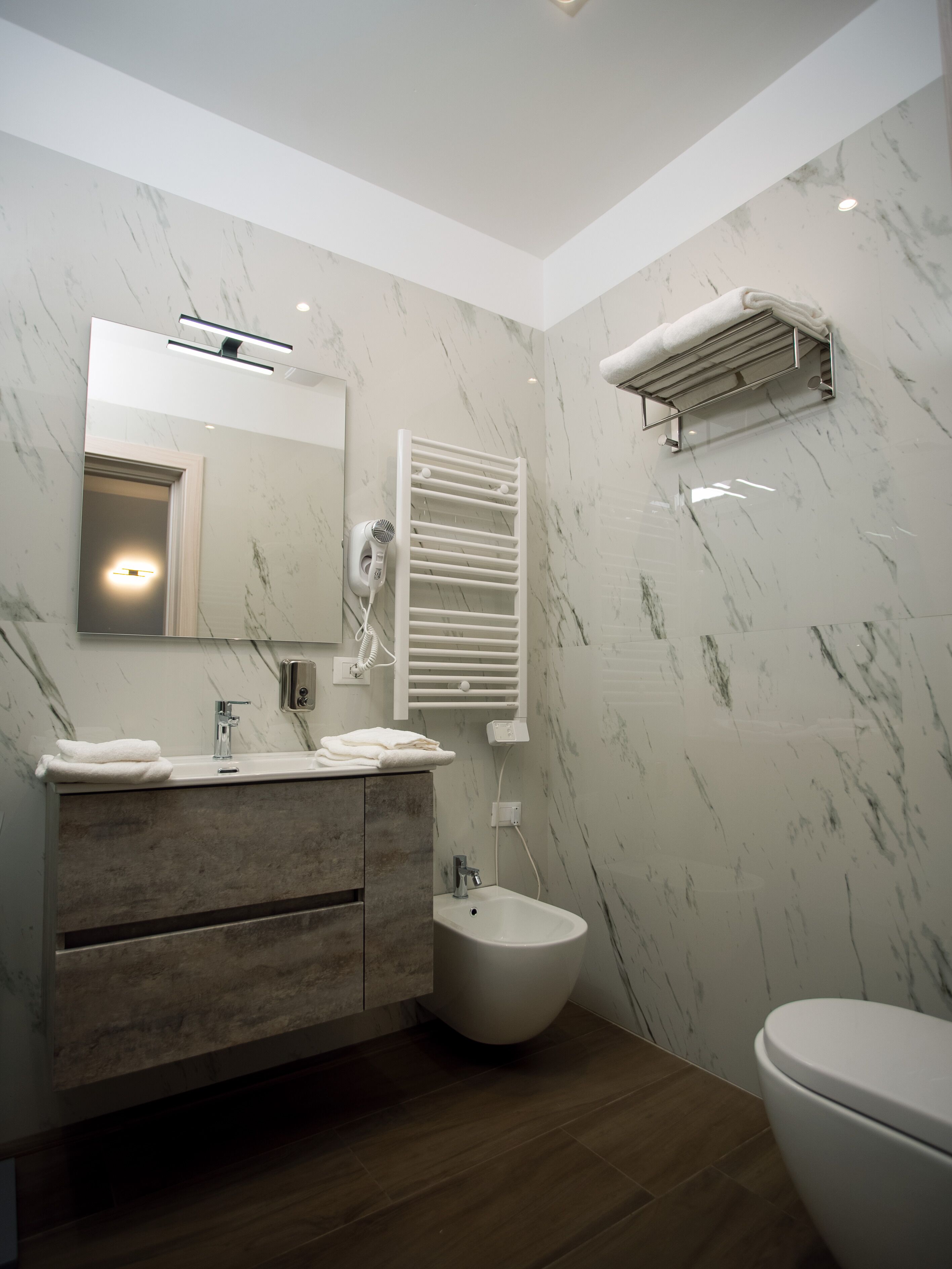 Un bany modern amb una paret de marbre, un lavabo amb rentapelats, un vàter i un lavabo.