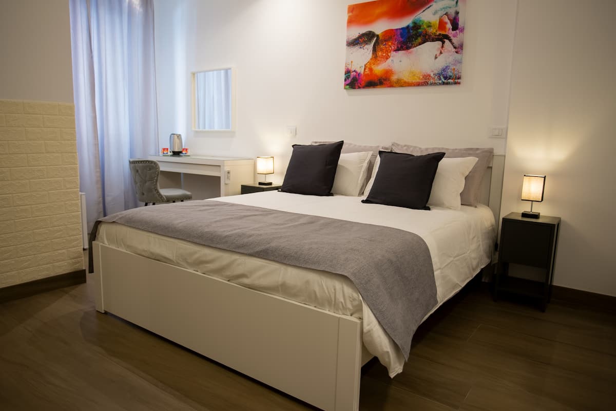 A modern hotel room with a large bed, bedside tables with lamps, a desk, and a chair.
