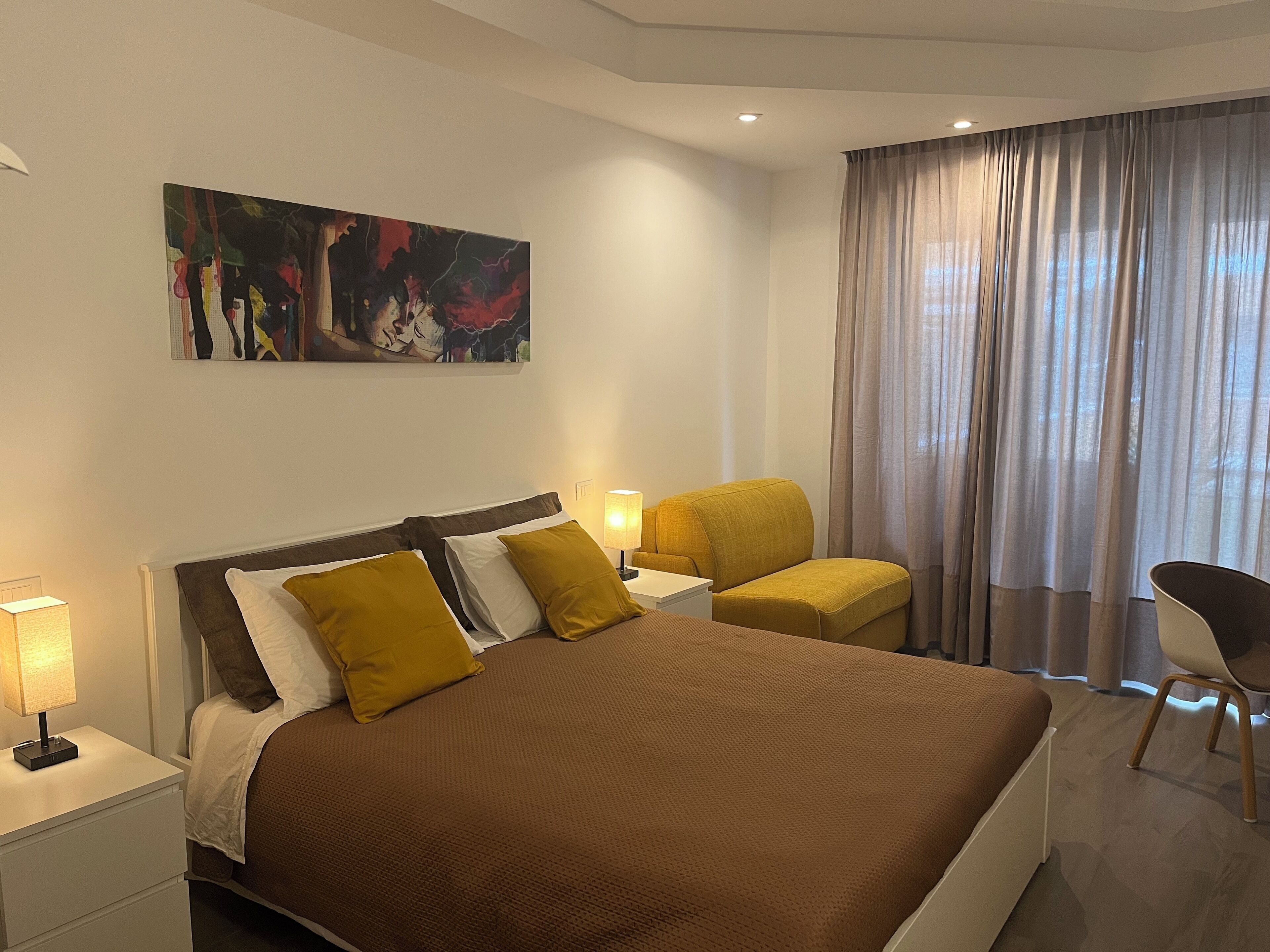 Una camera d'albergo moderna con un grande letto, una scrivania, una sedia e un quadro appeso alla parete.