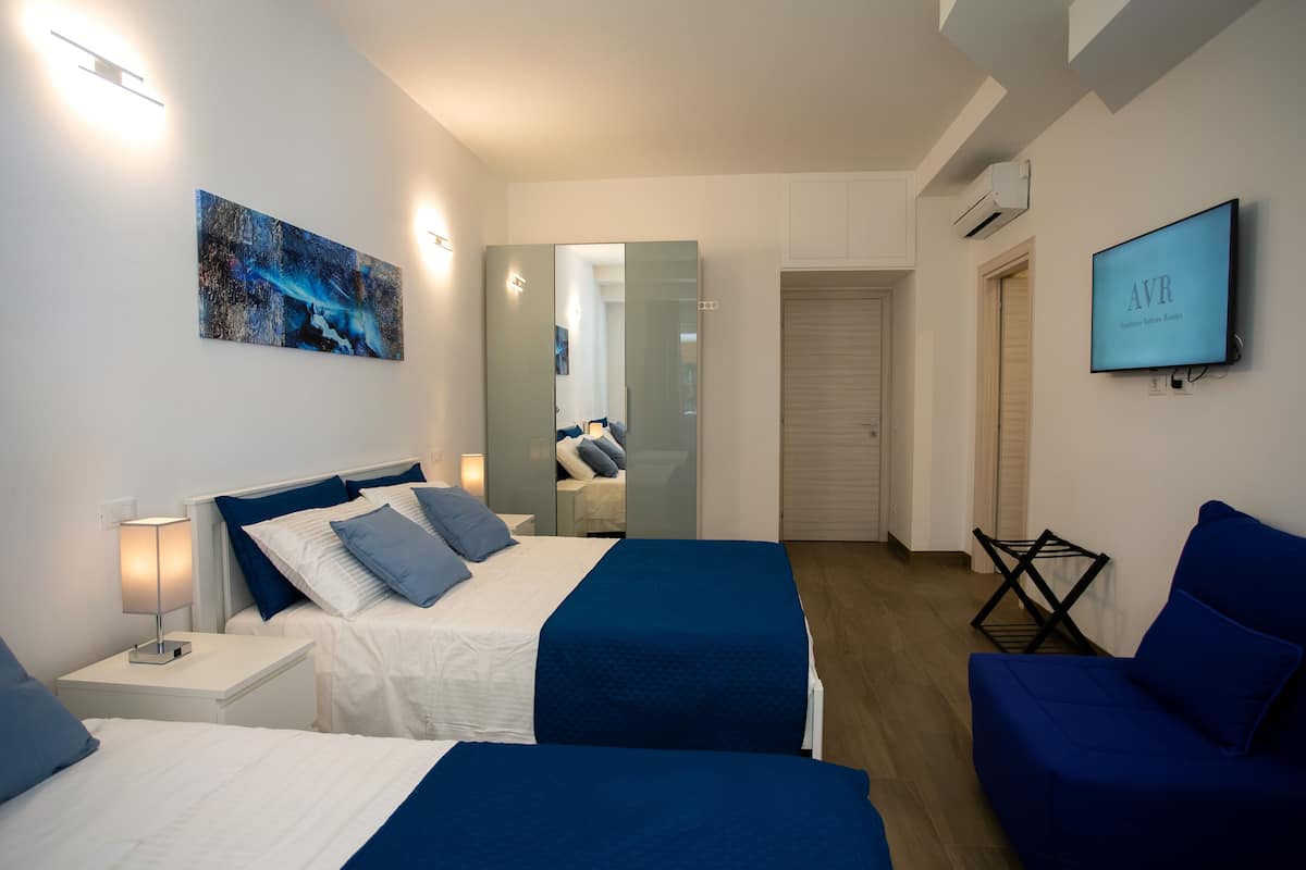 A hotel room with two beds, a TV, a painting, and a mirror.
