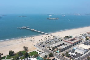 An aerial view of a coastal area with a beach, a pier, and a building complex.