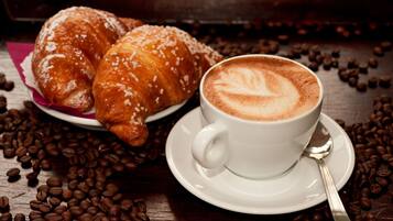 Un croissant et une tasse de café sur une table en bois, entourés de grains de café.