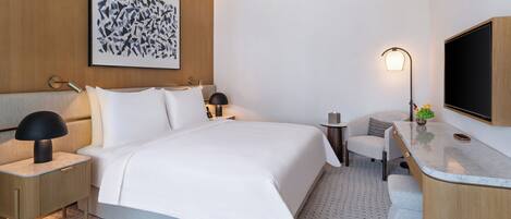 Una habitación de hotel moderna con una cama grande, mesitas de noche, un escritorio, una silla, un televisor y una obra de arte colgada en la pared.