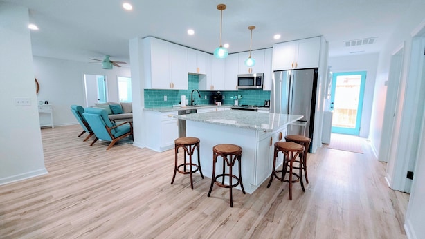 A modern kitchen with white cabinets, a central island with stools, a microwave, and a refrigerator.