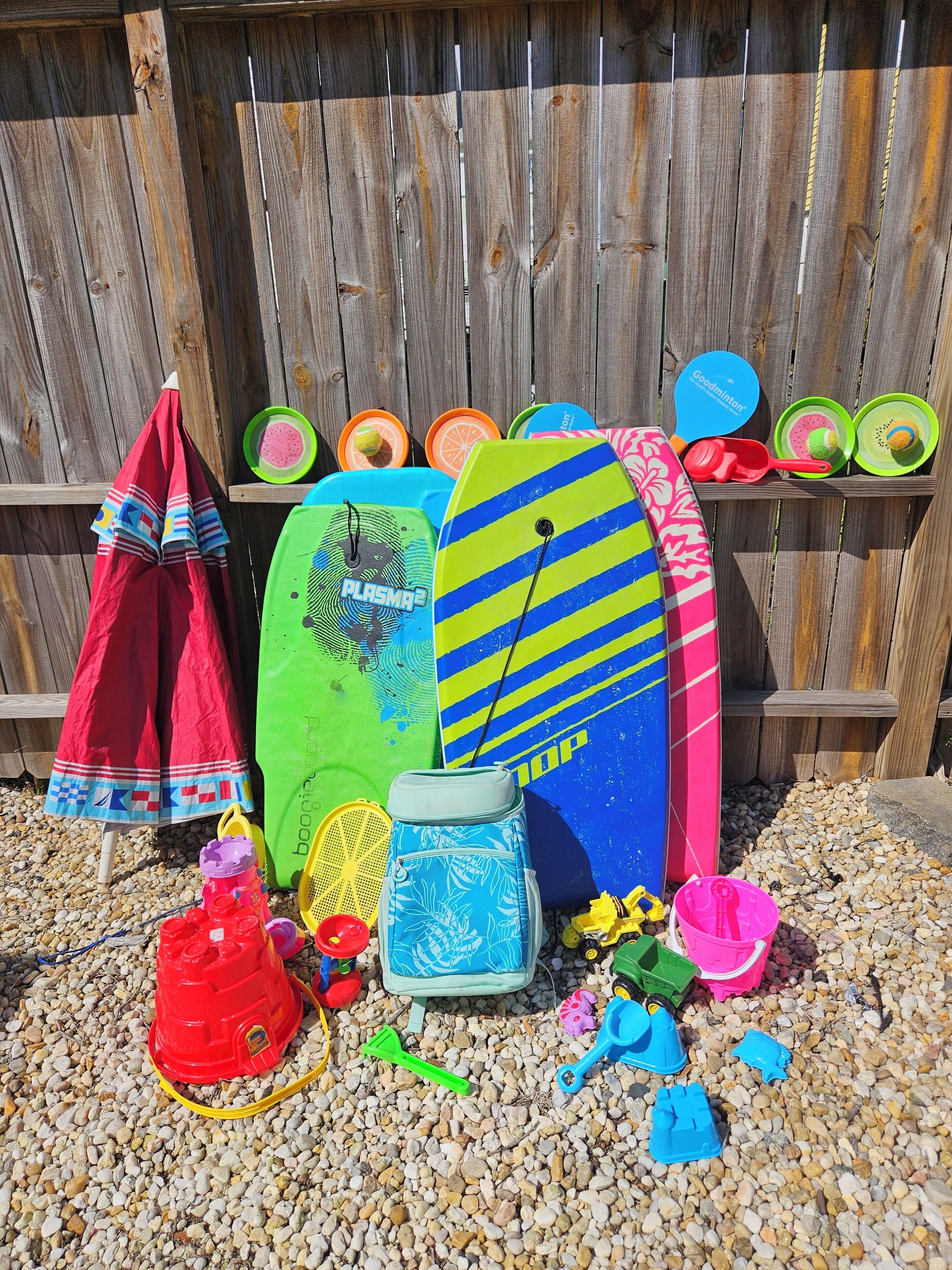 A collection of colorful beach toys and surfboards against a wooden fence.