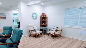 A spacious living room with a wooden floor, two armchairs, a small table, and a bookshelf.