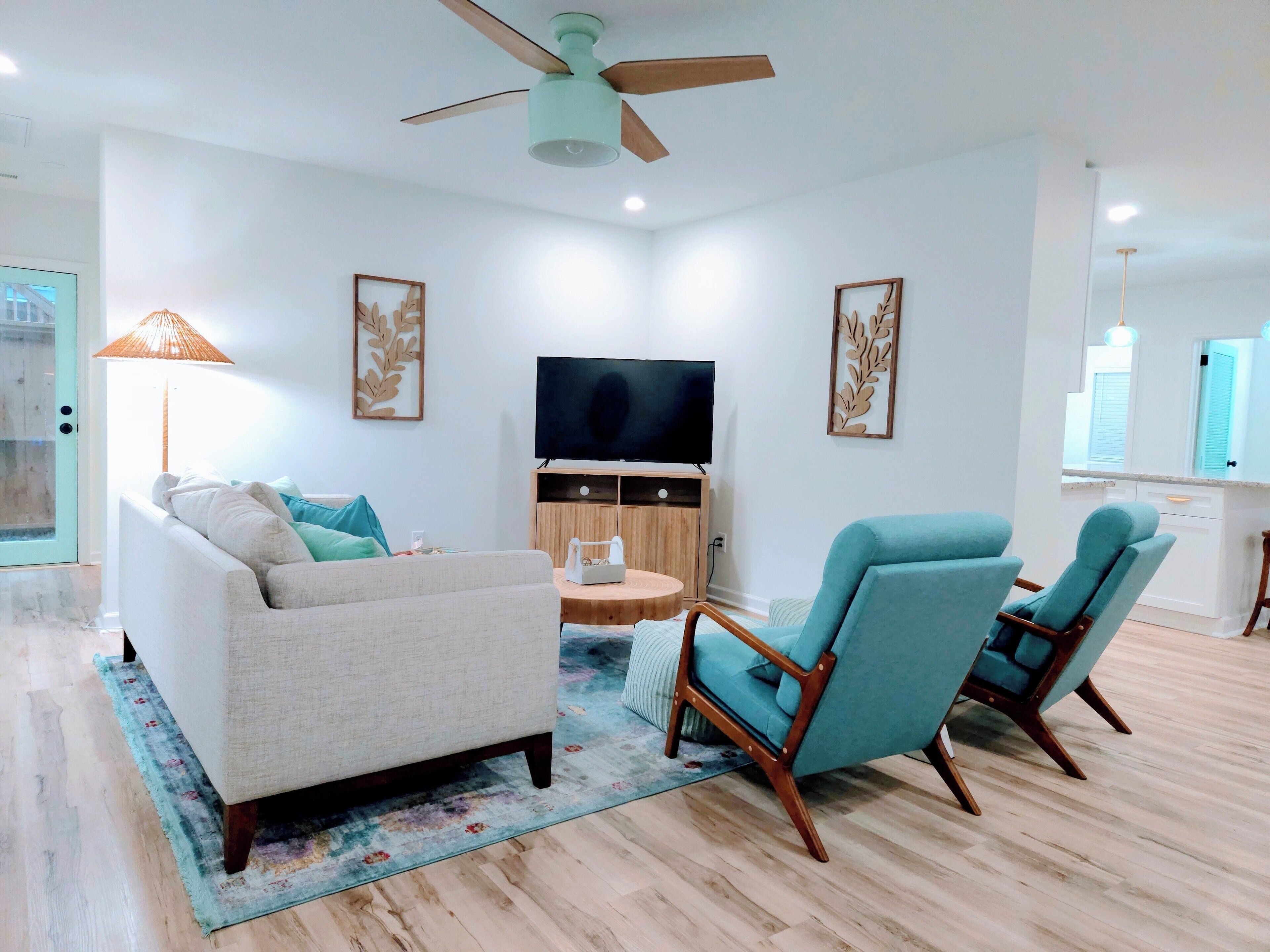 Una sala de estar moderna con un sofá, dos sillones, un televisor y un ventilador de techo.