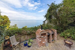 A brick-built outdoor oven with a chimney, surrounded by greenery and a wooden bench. - 5 Bed - Rose Cottage (Torquay)