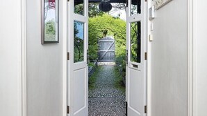 A hallway with a geometric patterned floor, a door leading to a garden, and a small outdoor area with a metal gate. - 5 Bed - Rose Cottage (Torquay)