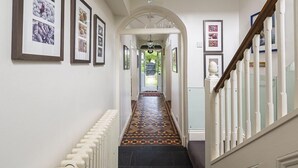 A hallway with a patterned floor, framed pictures on the walls, and a staircase with white railings. - 5 Bed - Rose Cottage (Torquay)