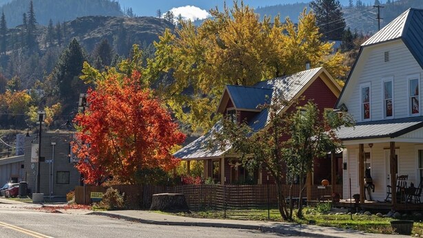 Pueblo pequeño con edificios residenciales y comerciales, una carretera despejada y montañas al fondo.