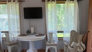 Comedor con mesa redonda, dos sillas, televisor montado en la pared y vista a zonas verdes.