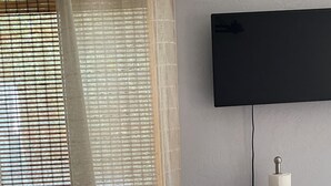 Una habitación con una silla blanca, una mesa con una vela y un televisor montado en la pared.