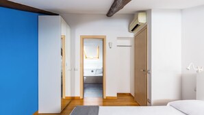 A bedroom with a bed, a wardrobe, a bathroom visible through an open door, and a wooden ceiling beam. - Attico al Duomo by Napoliapartments (Naples)