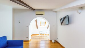 A hallway with a blue sofa, wooden flooring, a skylight, and a dining area with white chairs. - Attico al Duomo by Napoliapartments (Naples)