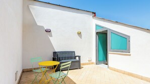 A small outdoor patio with a yellow table and two green chairs, a black bench, and a door leading to a room. - Attico al Duomo by Napoliapartments (Naples)