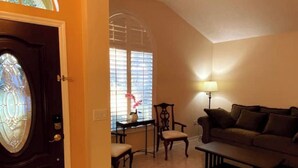 Un salon avec une porte en bois foncé, une fenêtre en verre, un canapé, une table basse et une lampe.