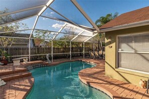 Une piscine couverte avec un espace patio, une clôture en bois et un bâtiment doté d’une fenêtre.