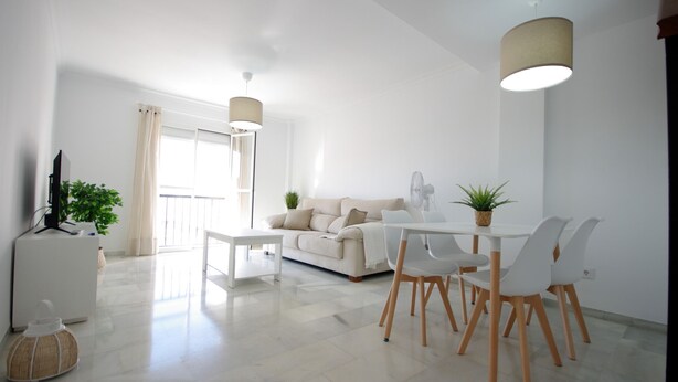 A modern living room with a white sofa, a dining table with chairs, a TV, and a plant. - 135 Livingtarifa Luna (Tarifa)