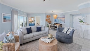 A spacious living room with a grey sofa, a round wooden coffee table, and a dining area with a white table and chairs.