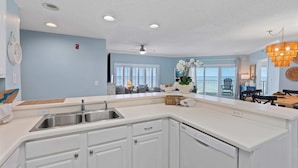 A modern kitchen with white cabinetry, a stainless steel sink, and a dining area with a view of the ocean.