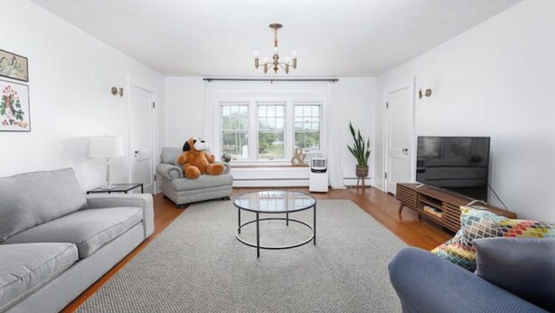 Ein geräumiges Wohnzimmer mit grauem Sofa, rundem Couchtisch, grauem Sessel, Fernseher und einem großen Fenster mit Tageslicht.