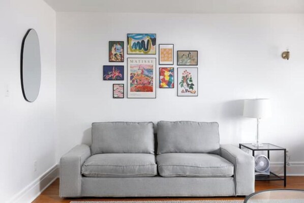 Ein modernes Wohnzimmer mit einem grauen Sofa, einem wandmontierten Spiegel und einer Reihe gerahmter Kunstwerke.