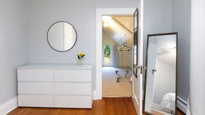 Ein Zimmer mit einer weißen Kommode, einem runden Spiegel und einer Tür zu einem Badezimmer.