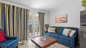 A living room with a sofa, a coffee table, a TV, and a balcony with curtains. - Beach Front- Cozy for Family In Casa Del Mar (Galveston)