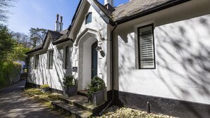 A white building with a steeply pitched roof, a chimney, and a small porch with steps. - 3 Bed Cove Cottage (Torquay)