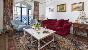 A room with a red sofa, a blue armchair, a wooden coffee table, and a view through a large window. - 3 Bed Cove Cottage (Torquay)