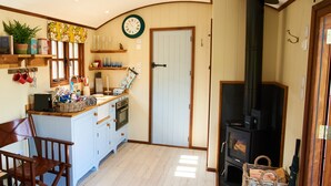 A cozy kitchen with a central island, wooden cabinets, a built-in oven, and a black wood stove. - Oak Shepherds Lodge (Dartmouth)