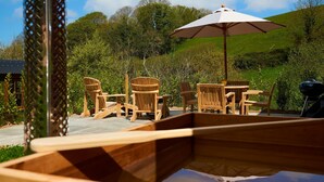 An outdoor seating area with wooden chairs and a table, an umbrella, and a grill. - Oak Shepherds Lodge (Dartmouth)