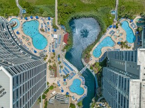 Un resort con varias piscinas, una fuente central y un paseo marítimo.