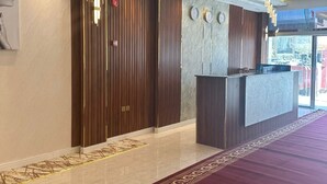 A hotel lobby with a reception desk, wooden paneling, clocks, and a patterned carpet.