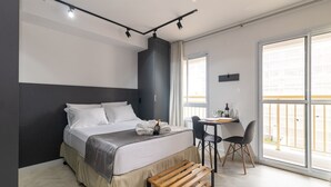 A modern bedroom with a bed, bedside table, and a small desk with chairs. - Estúdio Moderno com AC e Rooftop (São Paulo)