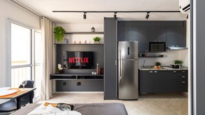 A modern kitchen with a built-in TV displaying "NETFLIX," a stainless steel refrigerator, and a microwave. - Estúdio Moderno com AC e Rooftop (São Paulo)