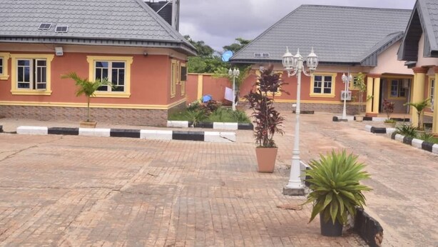 A paved courtyard with two buildings, each with a tiled roof and yellow-framed windows. - Mary queen hotels and suites  (Ekpoma)