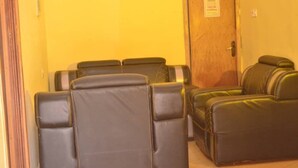 A room with two black leather sofas and a wooden door with a sign. - Mary queen hotels and suites  (Ekpoma)