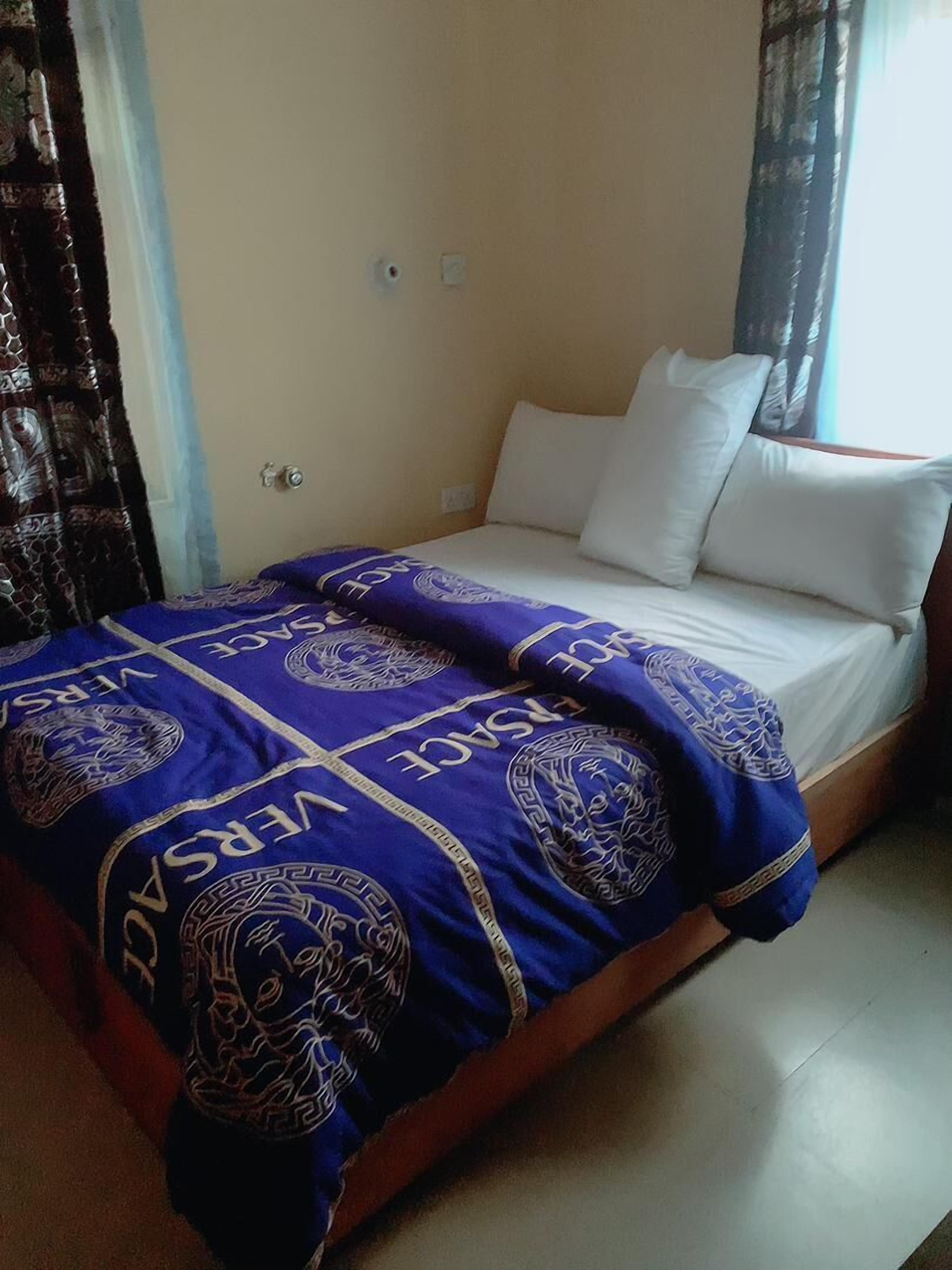 A bed with a white mattress and pillows, covered with a blue blanket featuring a geometric pattern.