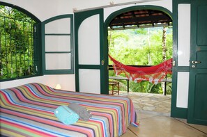 Une chambre avec un lit, un hamac et une vue sur la verdure.