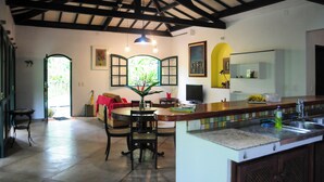 A spacious kitchen with a dining area, a large window, and a high ceiling with exposed beams. - Casa Caapuā, relax with comfort in nature. (Paraty)