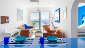 Una habitación de hotel moderna con comedor, sofá, mesa de centro y vista al mar.